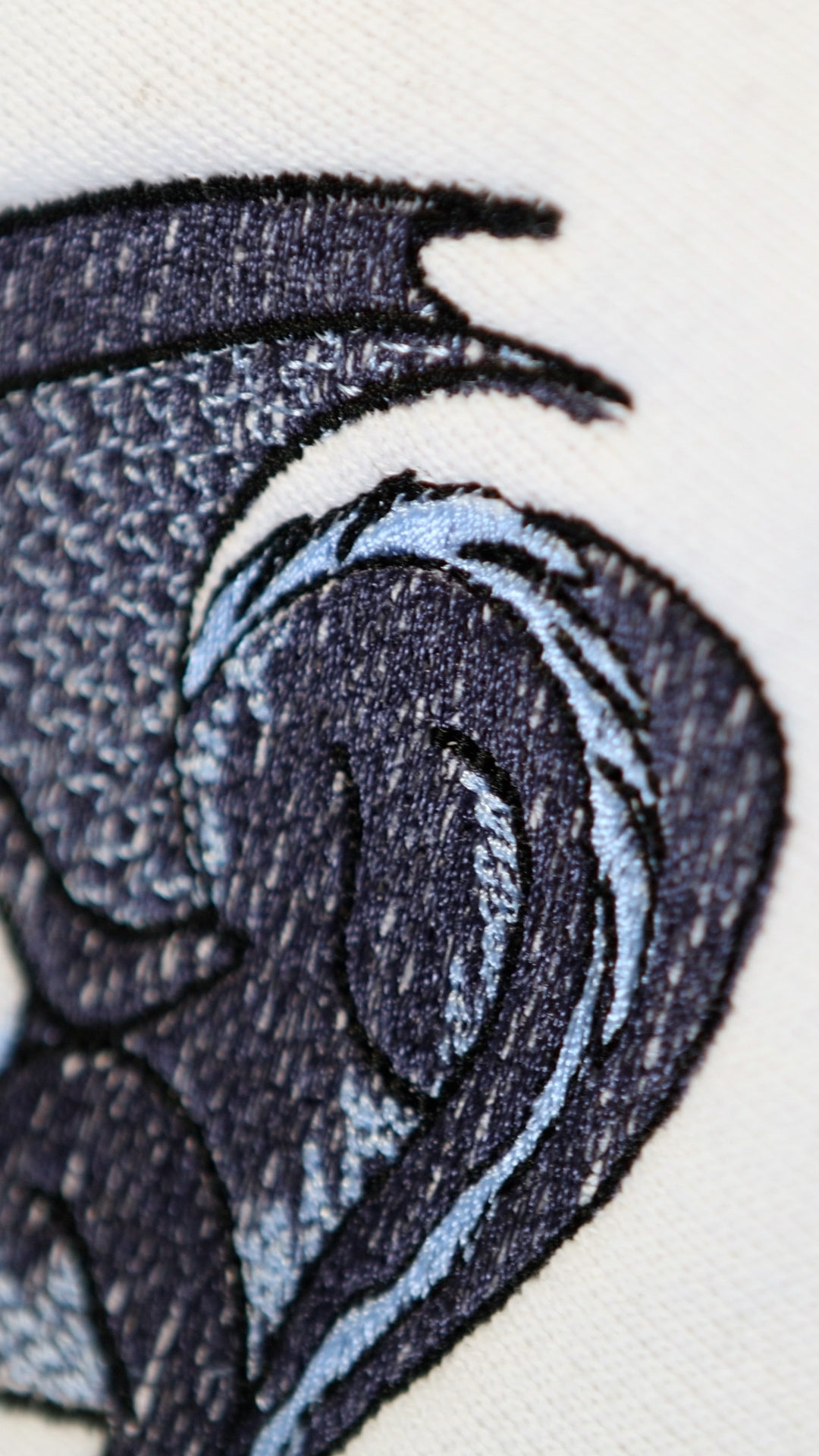 Close-up of the details of an embroidered black and blue dragon on a white crewneck sweatshirt